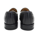 A black deerskin slip-on loafer with a tassel detail on the vamp, featuring a classic round toe and a low heel.