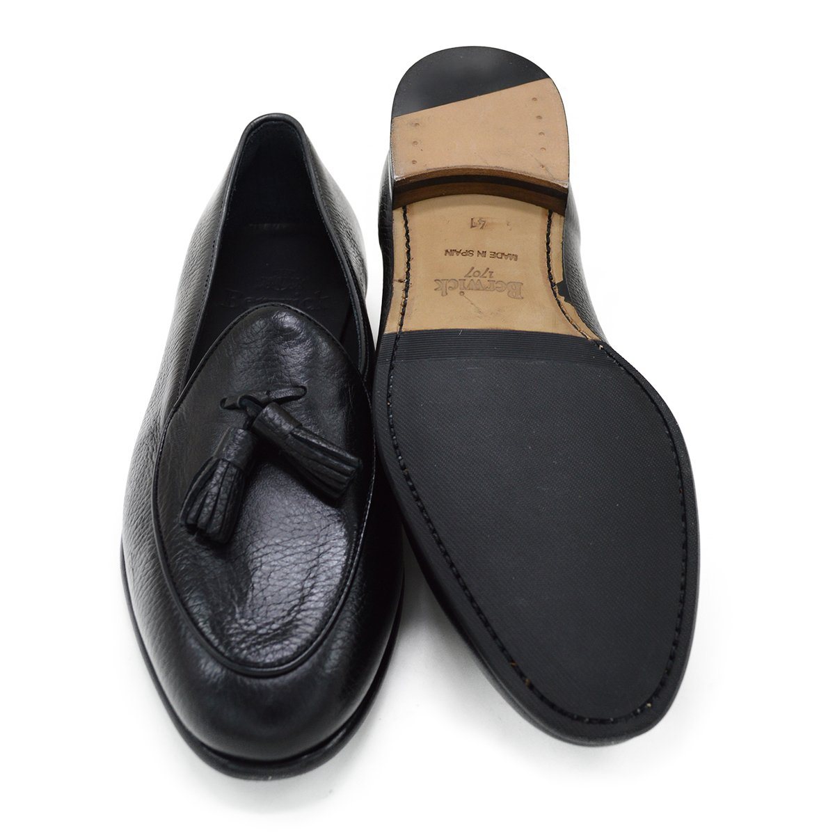 A black deerskin leather tassel Belgian loafer with an almond-shaped toe and a subtle tread sole, displayed against a white background.