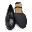A black deerskin leather tassel Belgian loafer with an almond-shaped toe and a subtle tread sole, displayed against a white background.