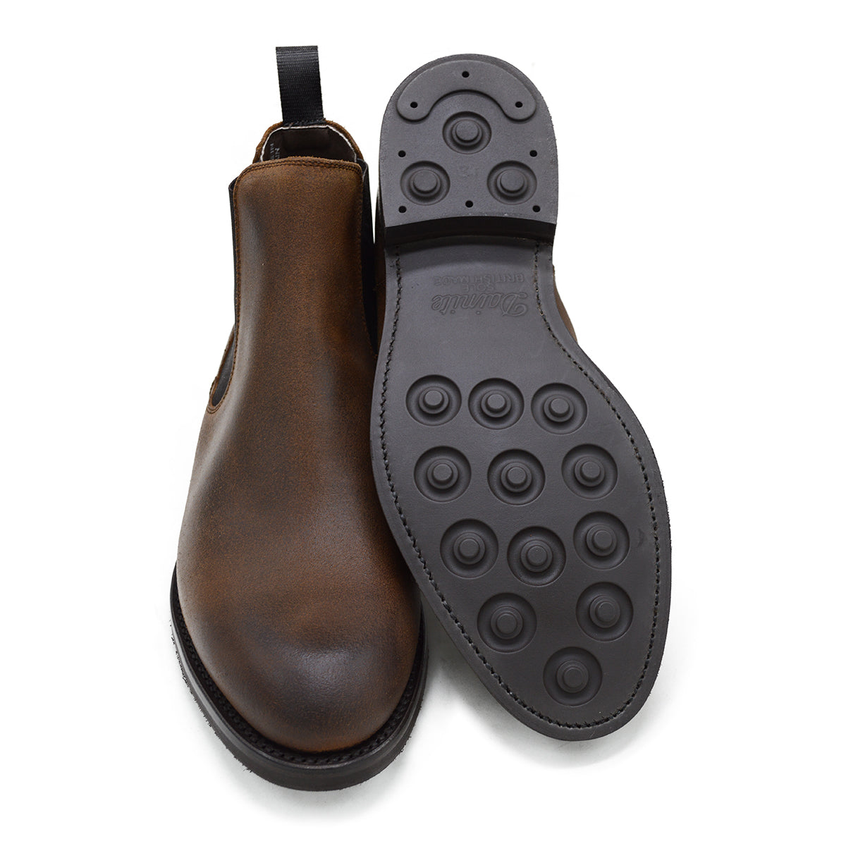 A dark brown Chelsea boot with a waxy leather finish and a contrasting black elastic side panel. The boot has a low heel and a small pull tab at the rear.