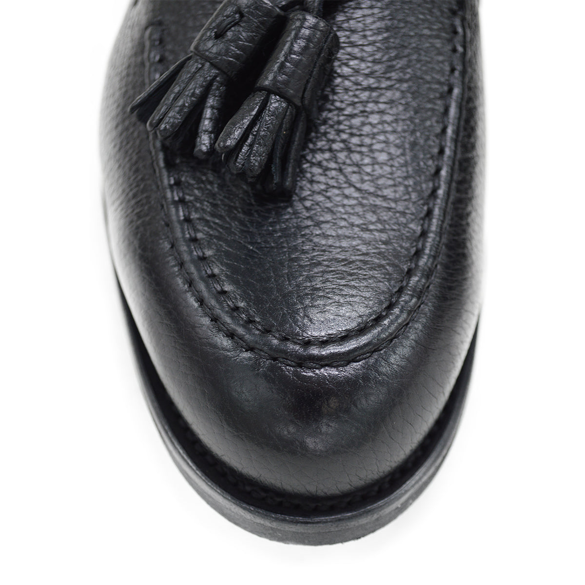 A black deerskin slip-on loafer with a tassel detail on the vamp, featuring a classic round toe and a low heel.
