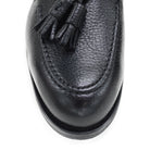 A black deerskin slip-on loafer with a tassel detail on the vamp, featuring a classic round toe and a low heel.