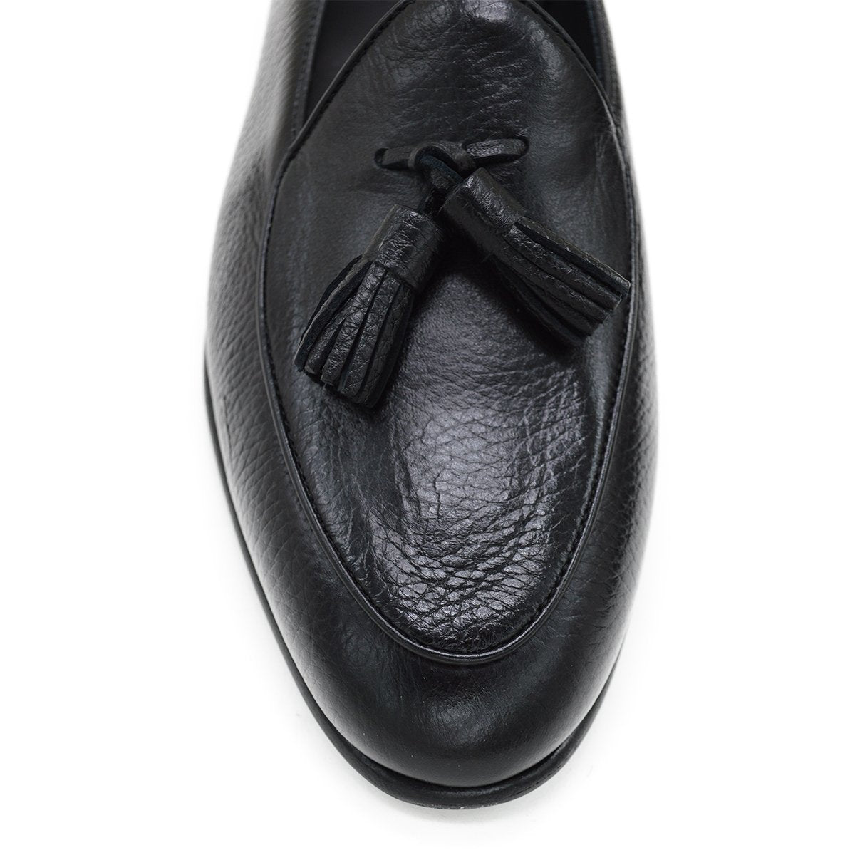 A black deerskin leather tassel Belgian loafer with an almond-shaped toe and a subtle tread sole, displayed against a white background.