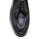 A black deerskin leather tassel Belgian loafer with an almond-shaped toe and a subtle tread sole, displayed against a white background.