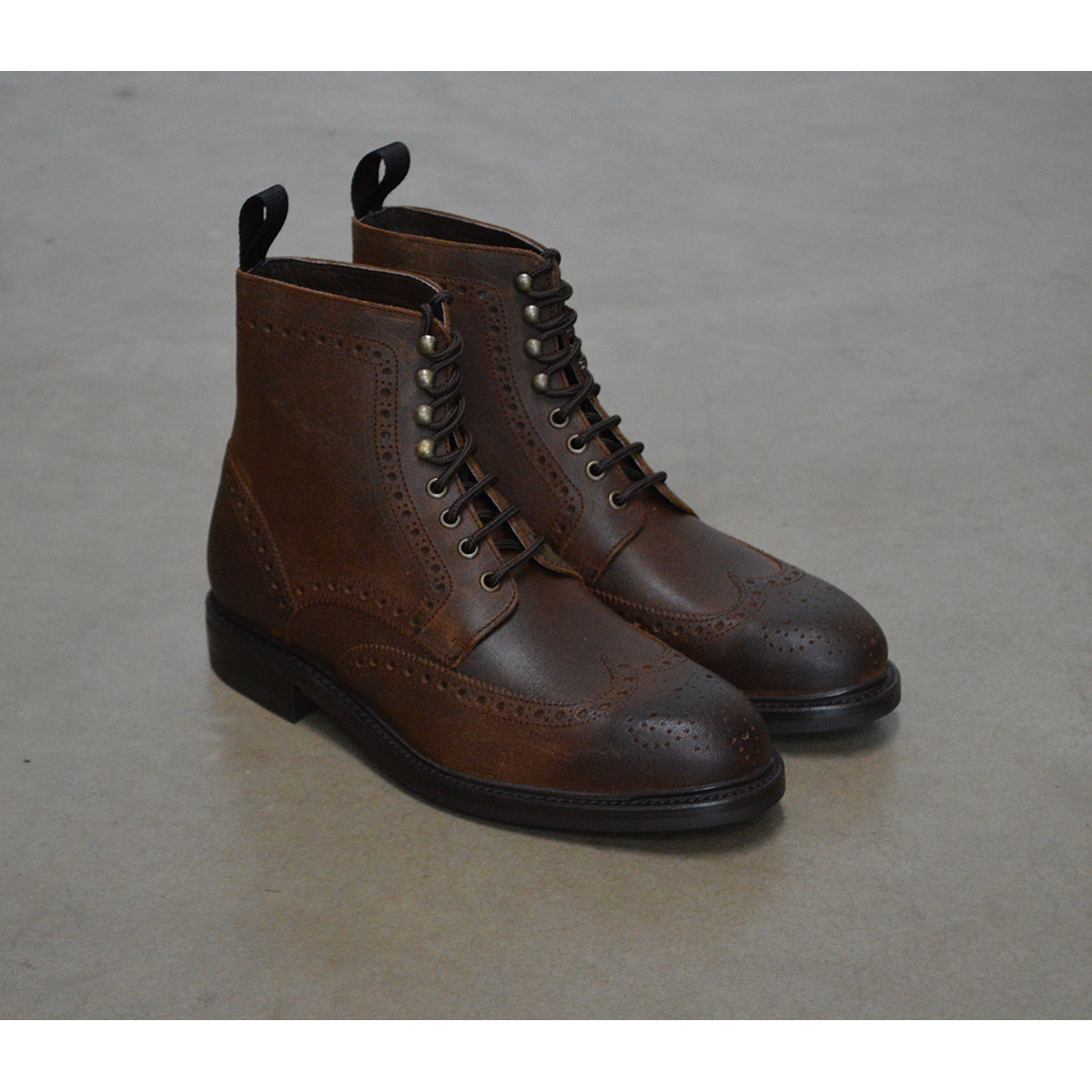 A dark brown lace-up brogue boot with a rubber sole and visible stitching on the upper part.