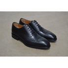 A Berwick 1707 black leather Oxford shoe with a chisel toe and lace-up closure with a Dainite rubber studded sole, on a polished concrete background.