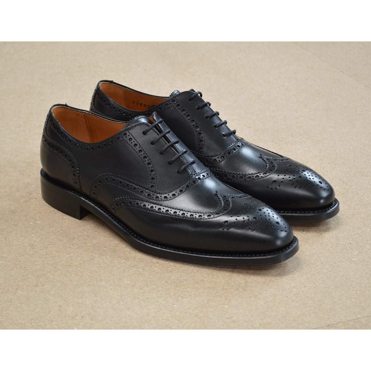 A Berwick 1707 black Oxford brogue shoe with brogue detailing and a lace-up closure. The shoe is made of smooth leather and appears to be sturdy and durable.