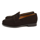 A dark brown suede penny loafer with a round toe shape and a studded Dainite sole.
