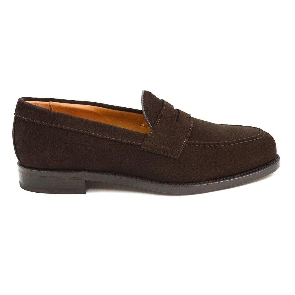A dark brown suede penny loafer with a round toe shape and a studded Dainite sole.