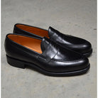 A black high-shine Berwick 1707 Penny Loafer with a round toe and Dainite rubber sole.