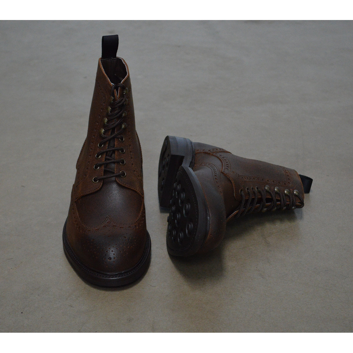 A dark brown lace-up brogue boot with a rubber sole and visible stitching on the upper part.