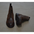 A dark brown lace-up brogue boot with a rubber sole and visible stitching on the upper part.