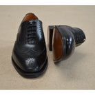 A Berwick 1707 black Oxford brogue shoe with brogue detailing and a lace-up closure. The shoe is made of smooth leather and appears to be sturdy and durable.