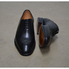 A black wholecut Oxford brogue shoe with a brogue pattern on the upper, a lace-up closure, and a goodyear welted leather sole.