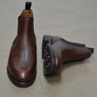 A dark brown grain leather Chelsea boot with a black elastic side panel and a round toe. The boot has a low heel and a goodyear welted dainite rubber sole.