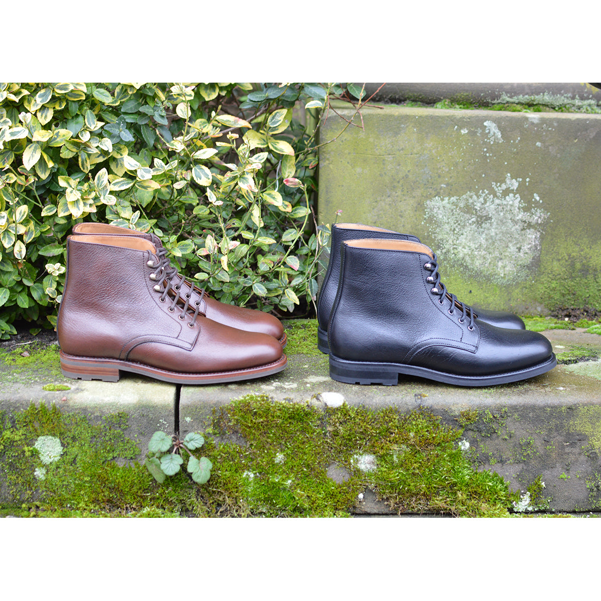 Pair of brown and black leather boots on a stone ledge with greenery in the background