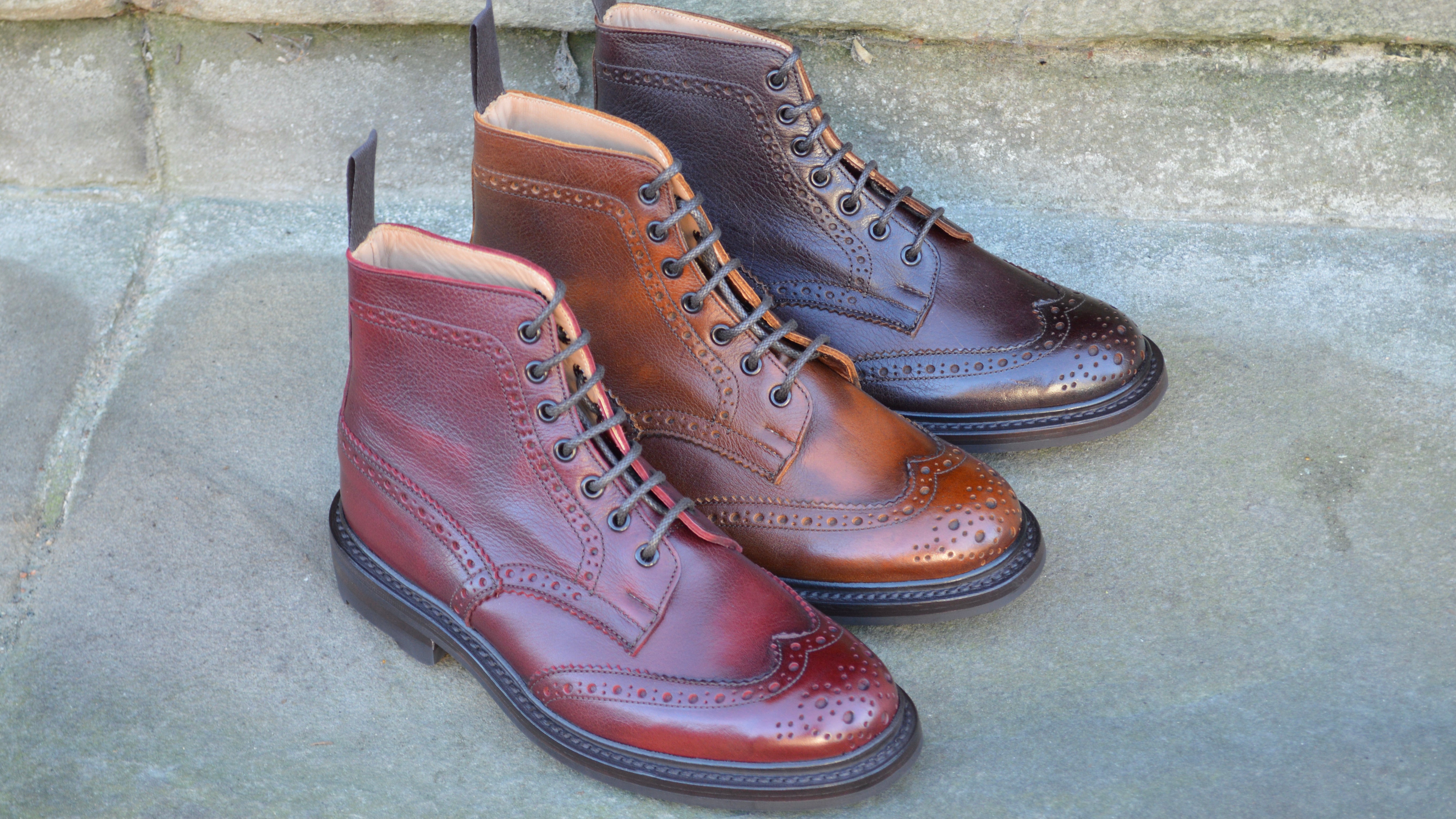 Tricker's Stow boots in various rich colours of Kudu leather on a heritage sandstone step