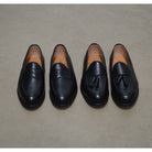 A black deerskin Penny loafer with a velvety soft texture and a classic round toe & Dainite sole, set against a polished concrete floor background.