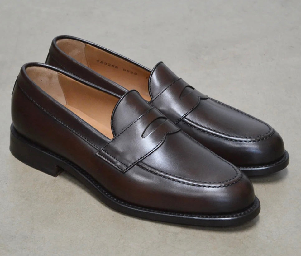 A dark brown Berwick 1707 Penny Loafer with a closed toe and loafers style heel, displayed on a polished concrete background.
