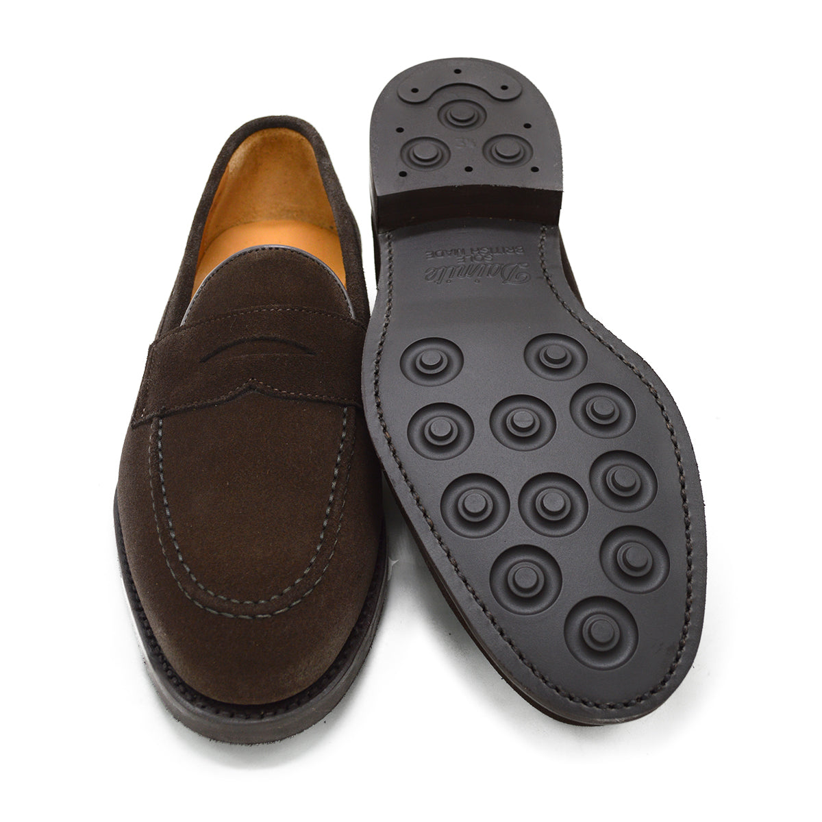A dark brown suede penny loafer with a round toe shape and a studded Dainite sole.