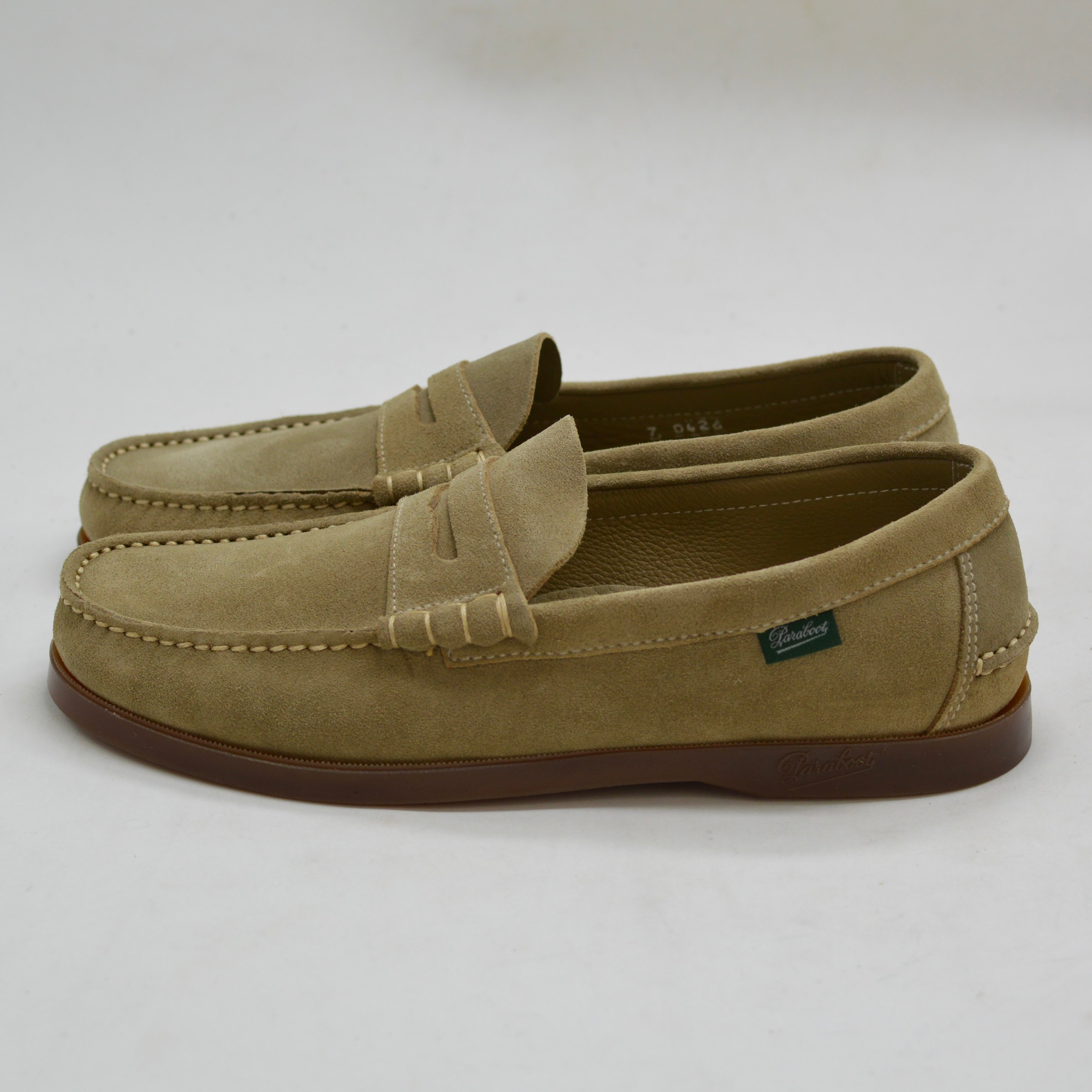 Pair of tan loafers with a brand logo on a light gray background