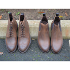 A dark brown lace-up brogue boot with a rubber sole and visible stitching on the upper part.