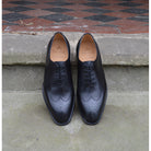 A black wholecut Oxford brogue shoe with a brogue pattern on the upper, a lace-up closure, and a goodyear welted leather sole.