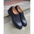 A black wholecut Oxford brogue shoe with a brogue pattern on the upper, a lace-up closure, and a goodyear welted leather sole.