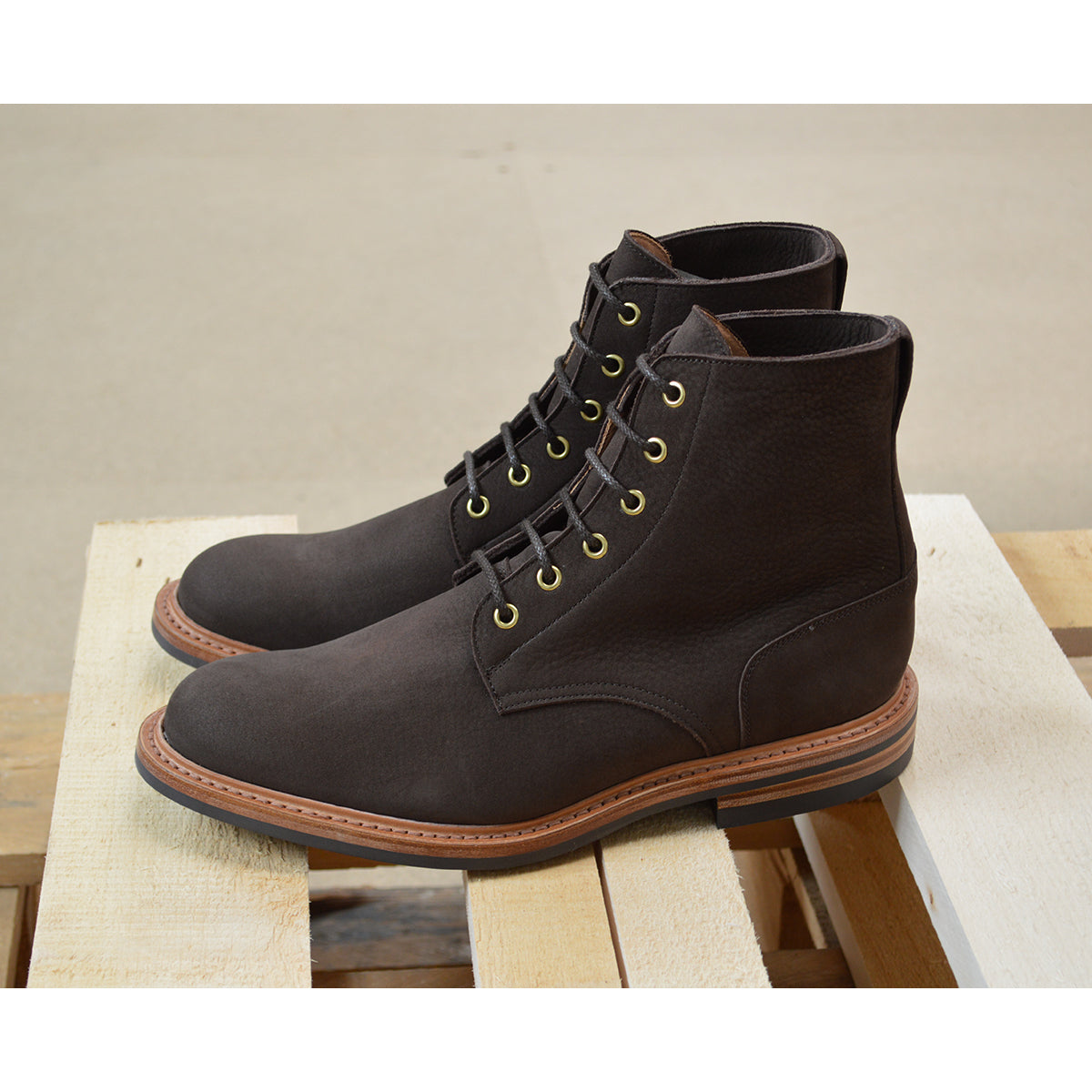 A dark brown Trickers Bernwood service boot made of Hydro Nubuck with a Dainite sole, featuring brass eyelets and a cream Barbour welt.