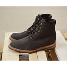 A dark brown Trickers Bernwood service boot made of Hydro Nubuck with a Dainite sole, featuring brass eyelets and a cream Barbour welt.