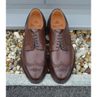 A Berwick 1707 brown brogue derby shoe with a round toe shape and lace-up closure. It features a grainy texture and brogue detailing & Dainite soles