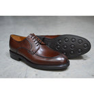 A pair of dark brown Berwick 1707 Split Toe Derby shoes with laces, set against a polished concrete background.