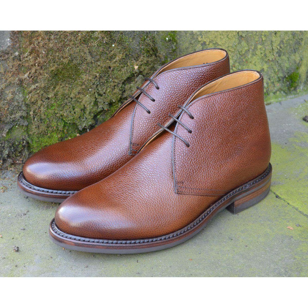A dark brown grain leather chukka boot with a round toe and goodyear welted dainite rubber sole.