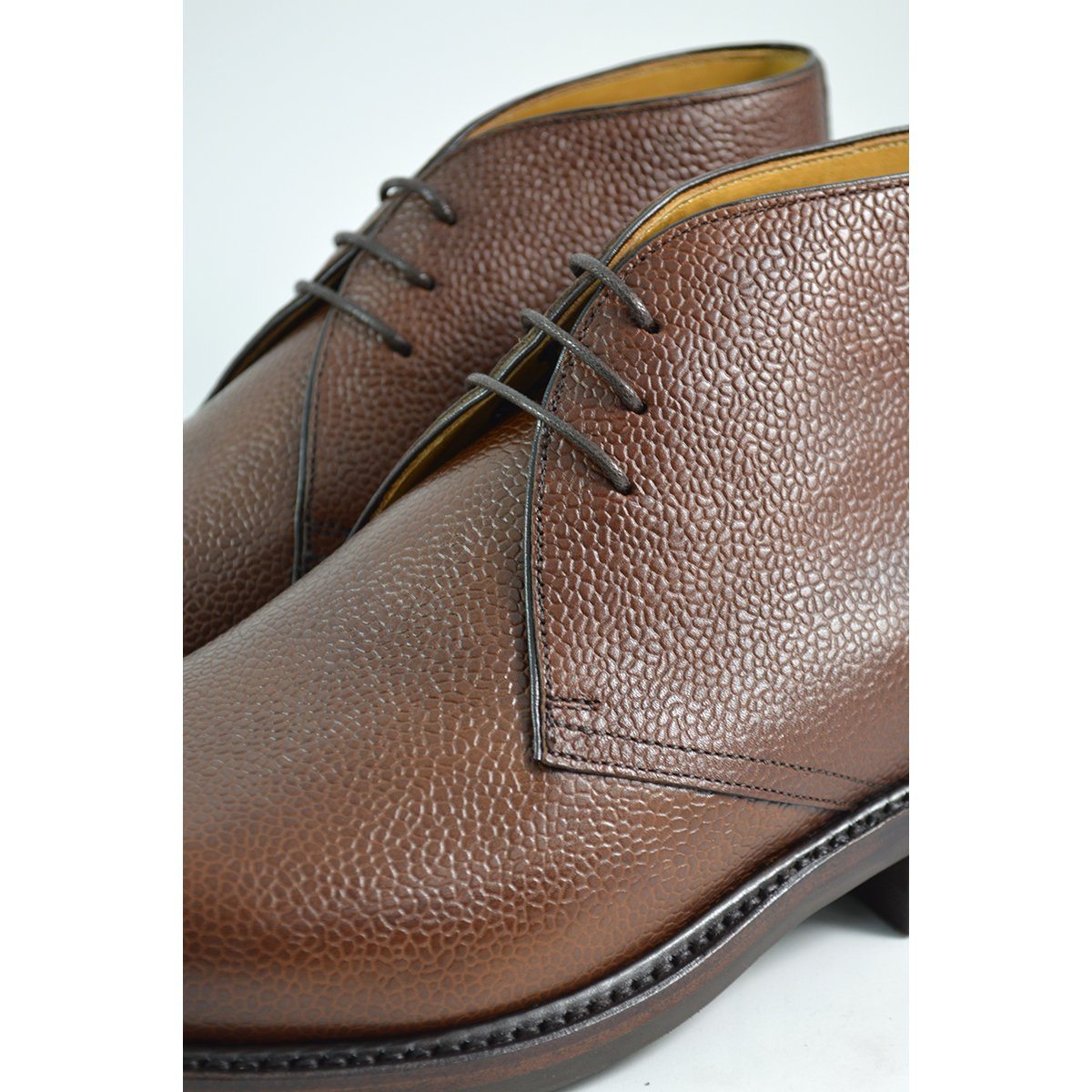 A dark brown grain leather chukka boot with a round toe and goodyear welted dainite rubber sole.