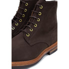 A dark brown Trickers Bernwood service boot made of Hydro Nubuck with a Dainite sole, featuring brass eyelets and a cream Barbour welt.