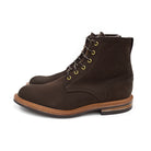 A dark brown Trickers Bernwood service boot made of Hydro Nubuck with a Dainite sole, featuring brass eyelets and a cream Barbour welt.
