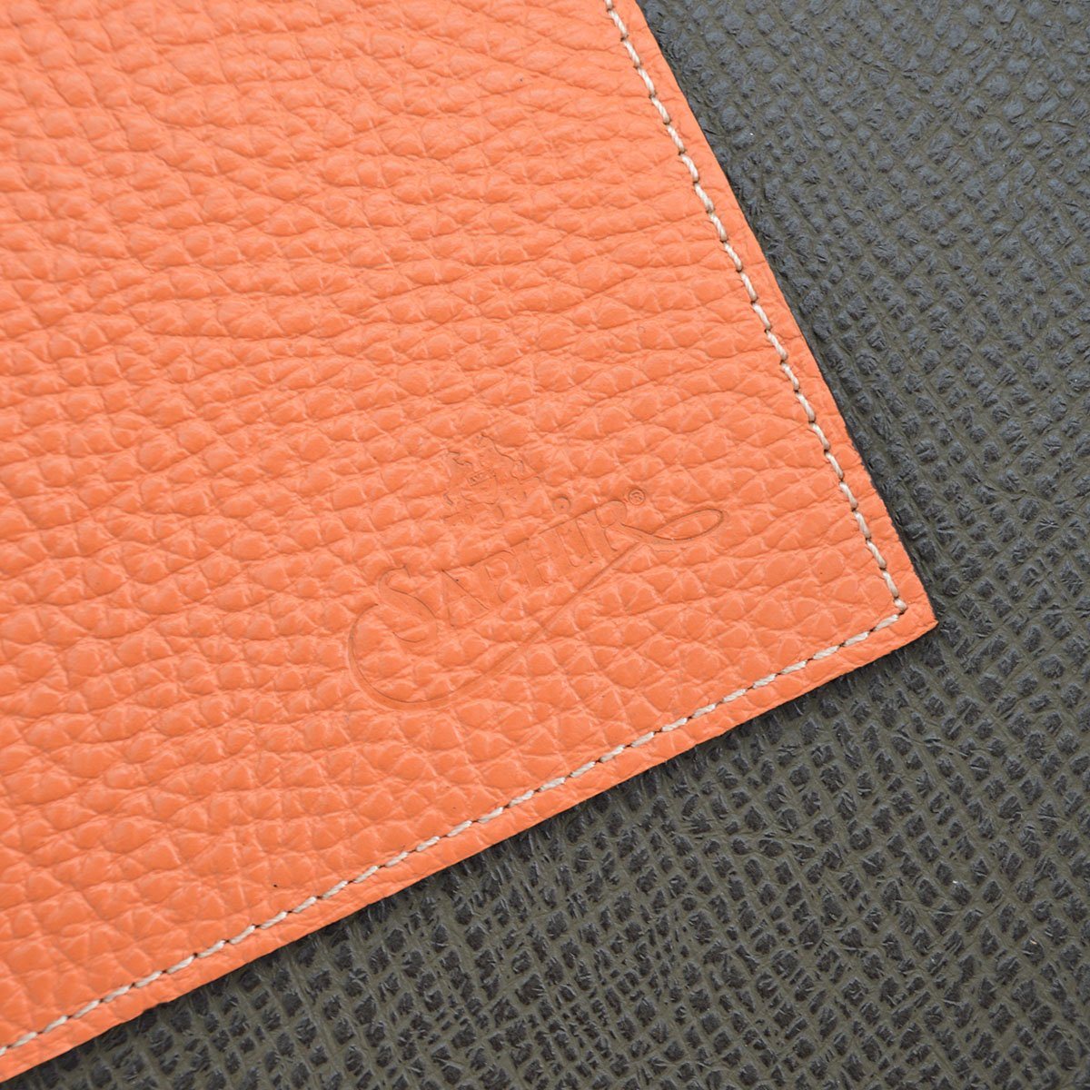 A Saphir Medaille D'Or rolled-up orange leather shoeshine mat with a nickel stud on the exterior.