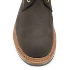 A dark brown Trickers Bernwood service boot made of Hydro Nubuck with a Dainite sole, featuring brass eyelets and a cream Barbour welt.
