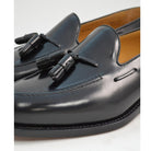 A black tasselled slip-on shoe with a high shine finish and a classic round toe.