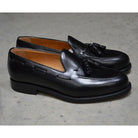 A black tasselled slip-on shoe with a high shine finish and a classic round toe.