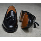 A black tasselled slip-on shoe with a high shine finish and a classic round toe.
