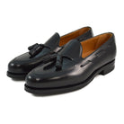 A black tasselled slip-on shoe with a polished, smooth upper and a classic round toe. The shoe is set against a white background.