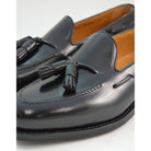 A black tasselled slip-on shoe with a polished, smooth upper and a classic round toe. The shoe is set against a white background.