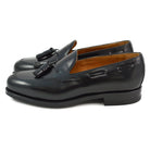 A black tasselled slip-on shoe with a polished, smooth upper and a classic round toe. The shoe is set against a white background.