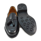A black tasselled slip-on shoe with a polished, smooth upper and a classic round toe. The shoe is set against a white background.