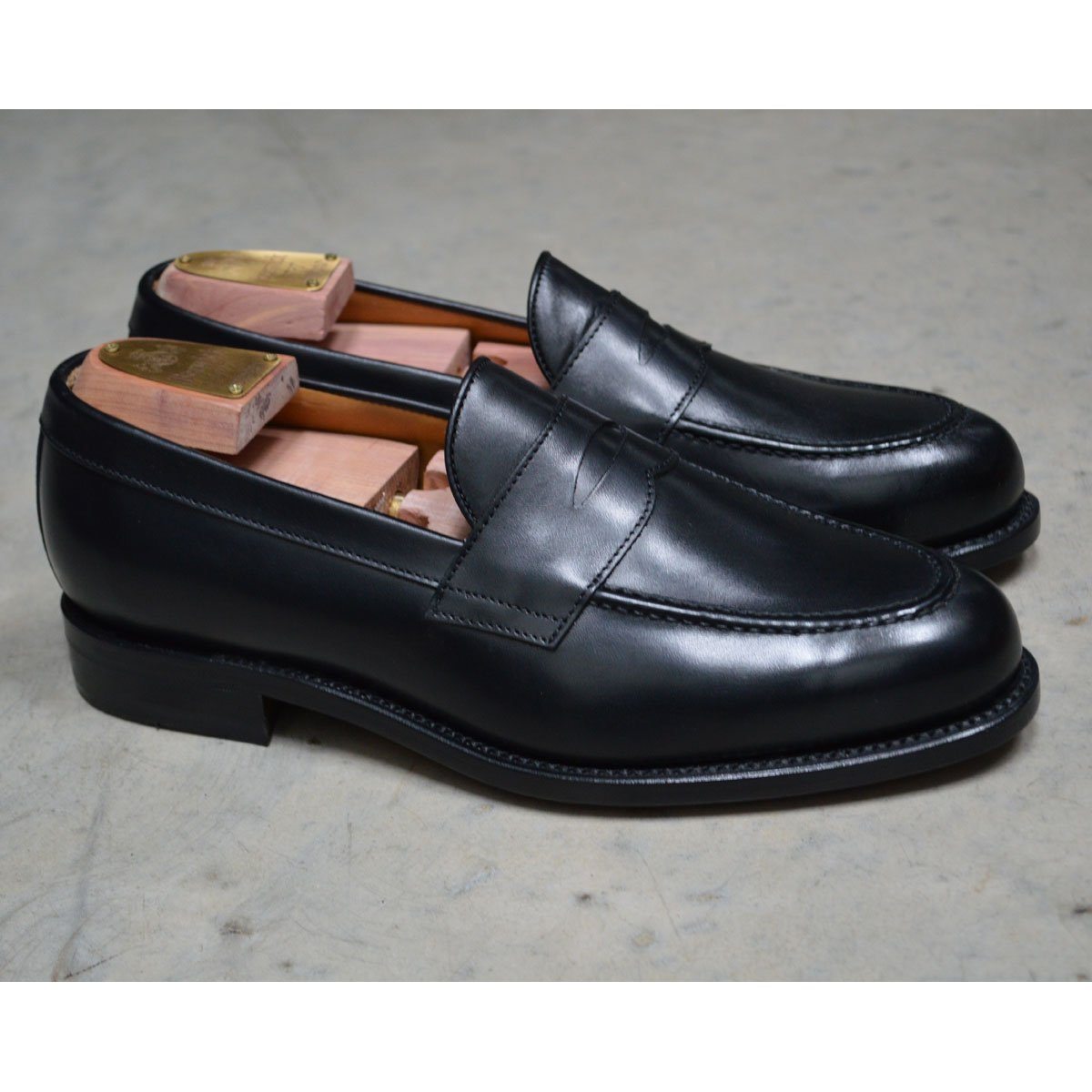 A classic black leather penny loafer shoe for men, with a closed vamp and a low heel.