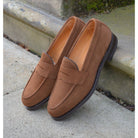 A brown suede penny loafer with a Dainite rubber sole, showing a classic round toe shape and a signature penny slot detail & Dainite Soles