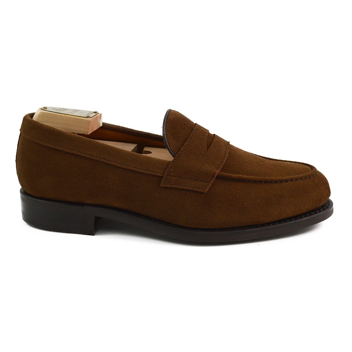 A brown suede penny loafer with a Dainite rubber sole, showing a classic round toe shape and a signature penny slot detail.