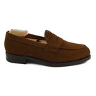 A brown suede penny loafer with a Dainite rubber sole, showing a classic round toe shape and a signature penny slot detail.