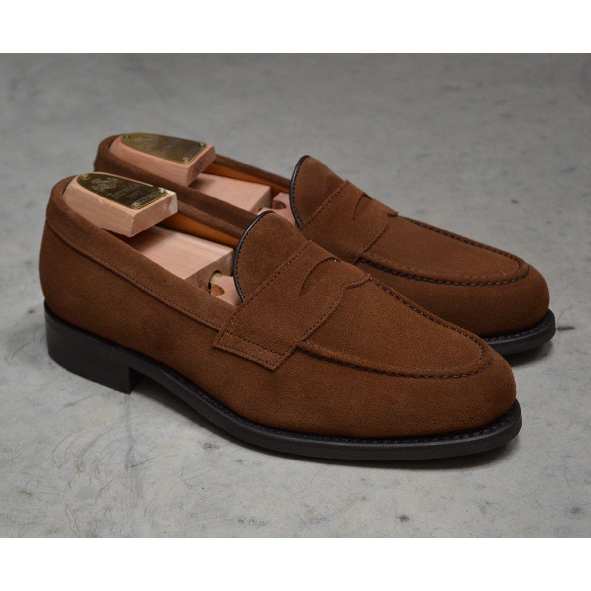 A brown suede penny loafer with a Dainite rubber sole, showing a classic round toe shape and a signature penny slot detail & Dainite Soles